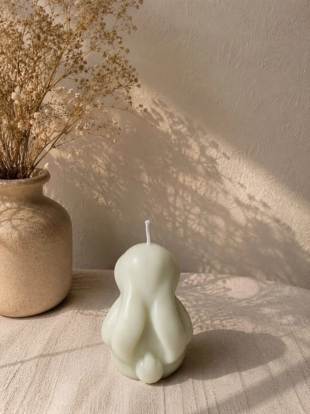 Sage green rounded candle beside a stoneware vase