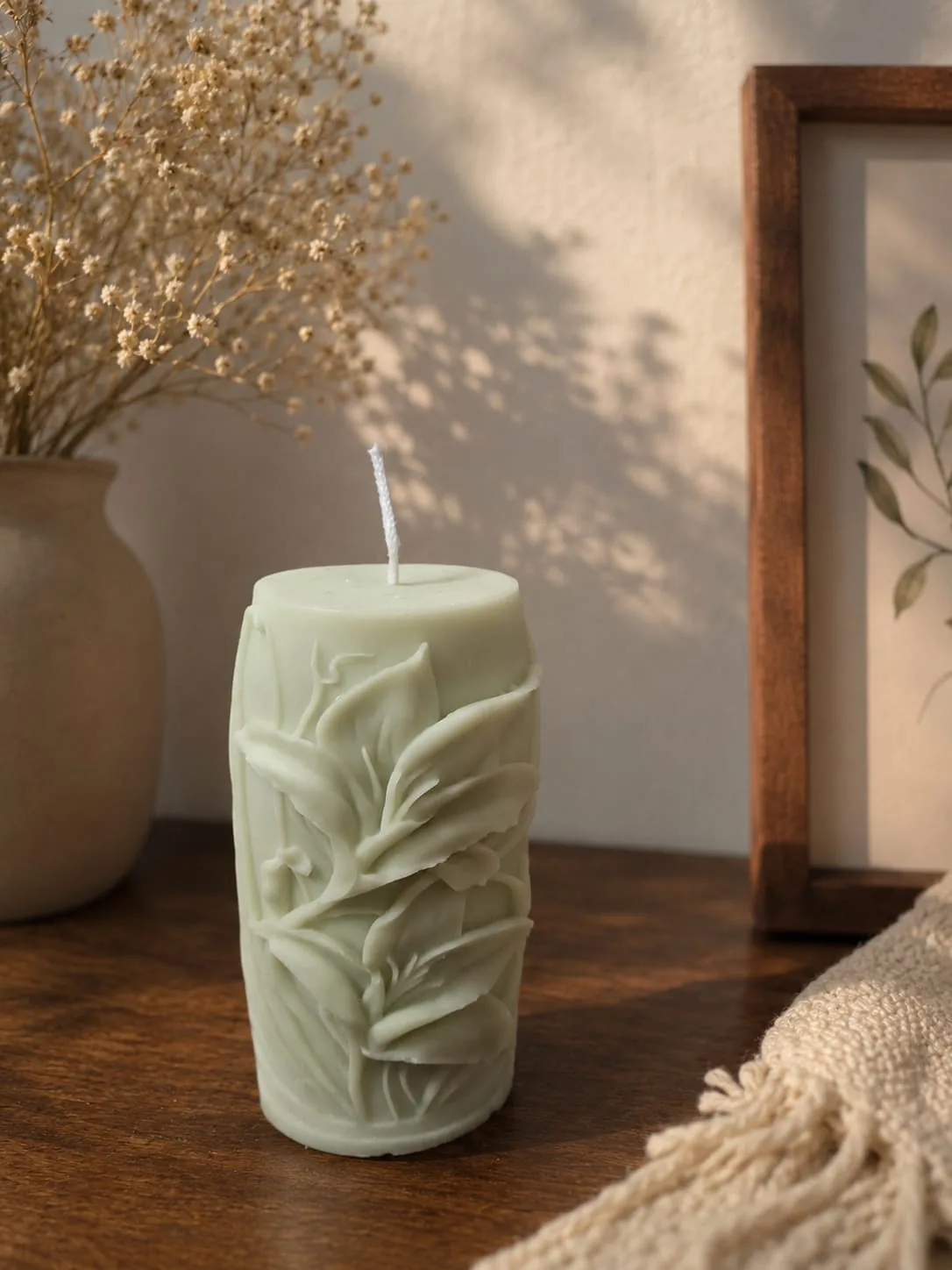 Sage green pillar candle with a carved floral relief