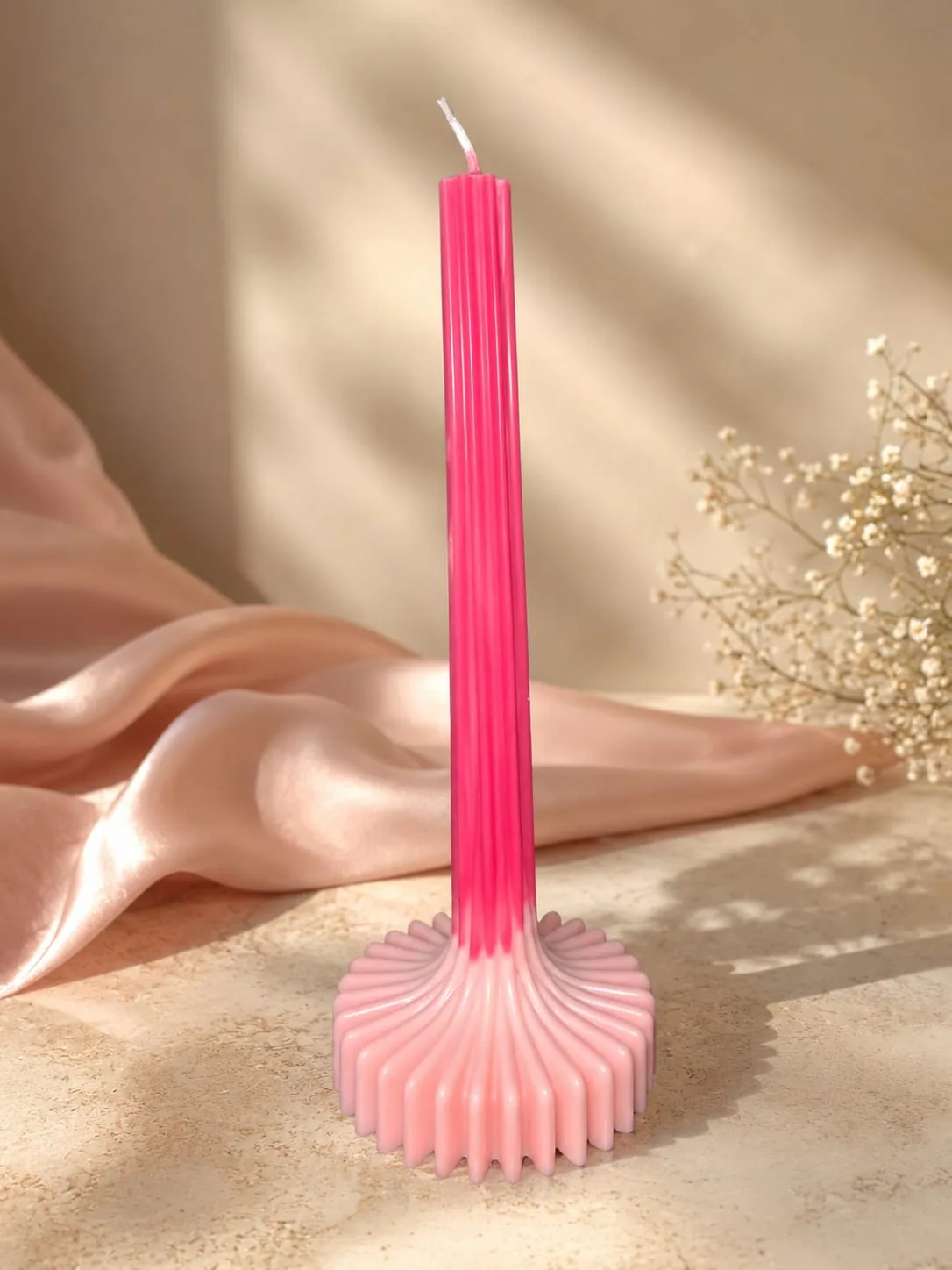 Tall pink candle on a fluted base against draped silk