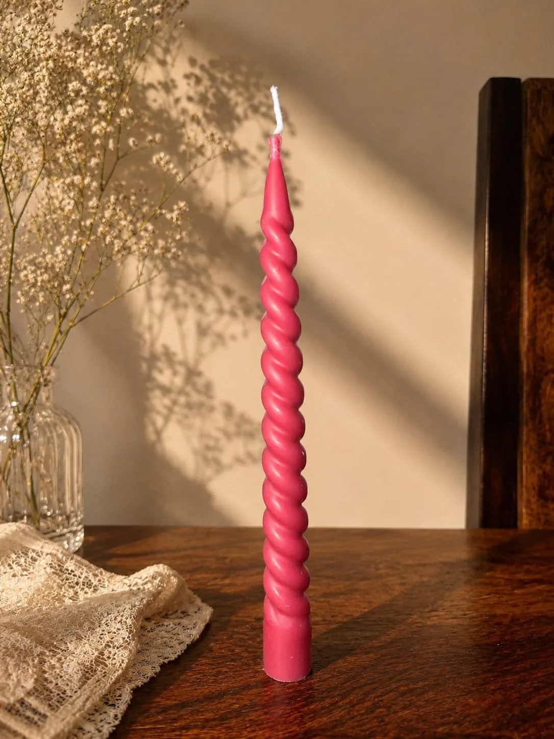Pink spiral twisted taper candle against a sunlit wall